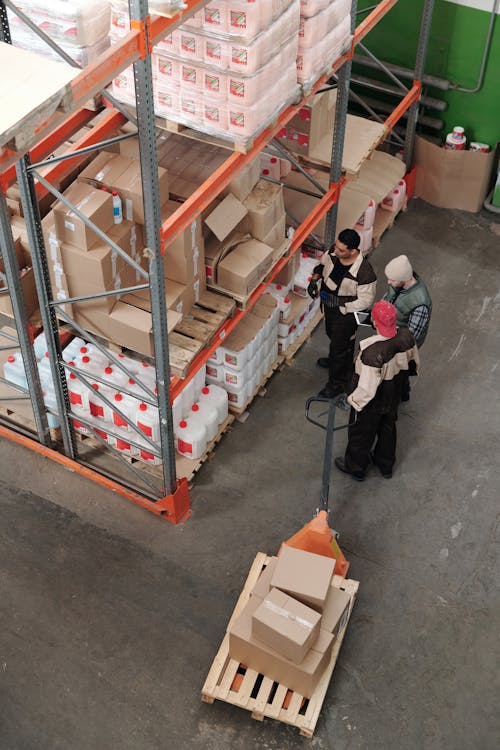Top-down view of three people inspecting a warehouse shelf loaded with boxes. Image by Tiger Lily on Pexels.